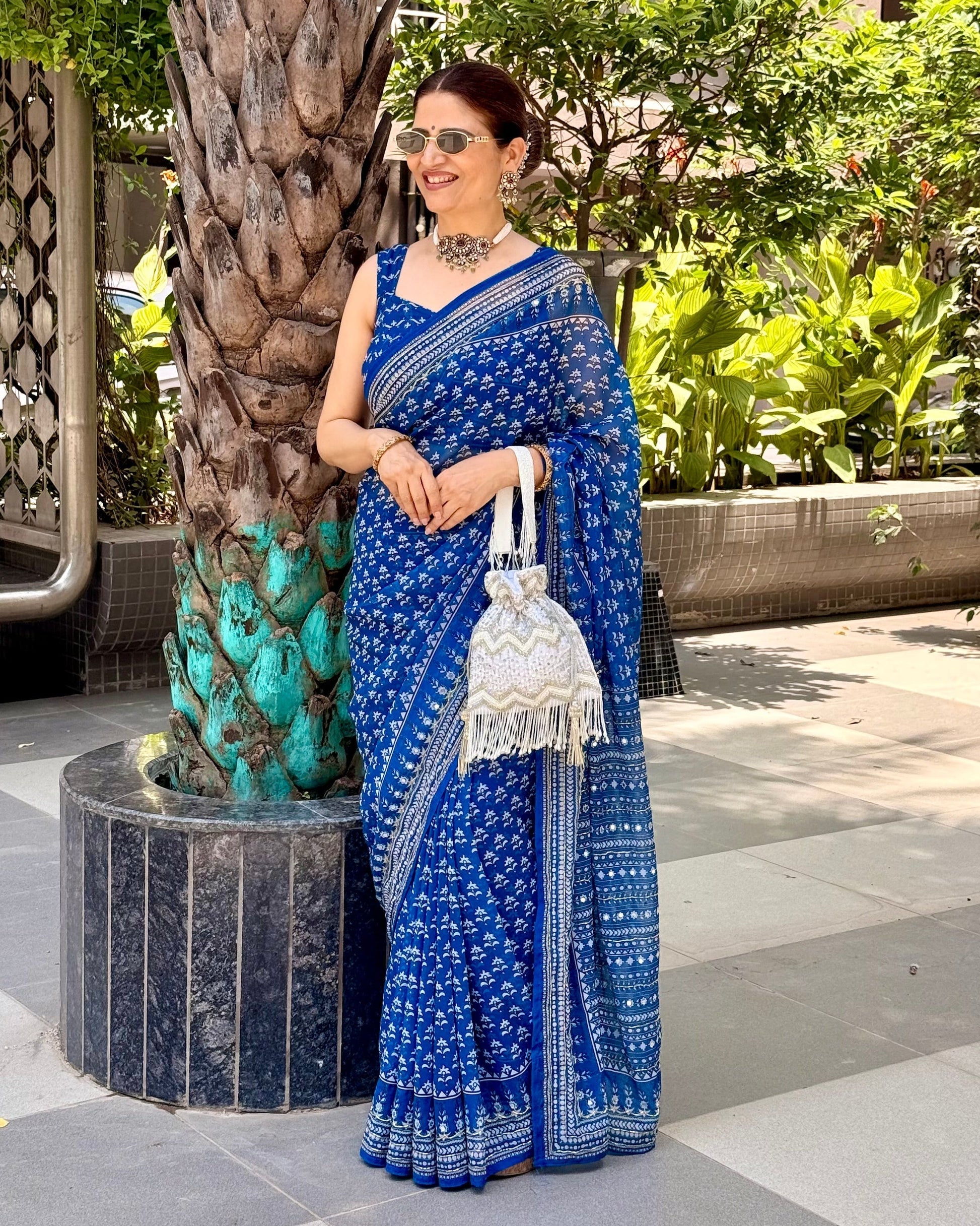 Woman in a blue saree standing outdoors with greenery around