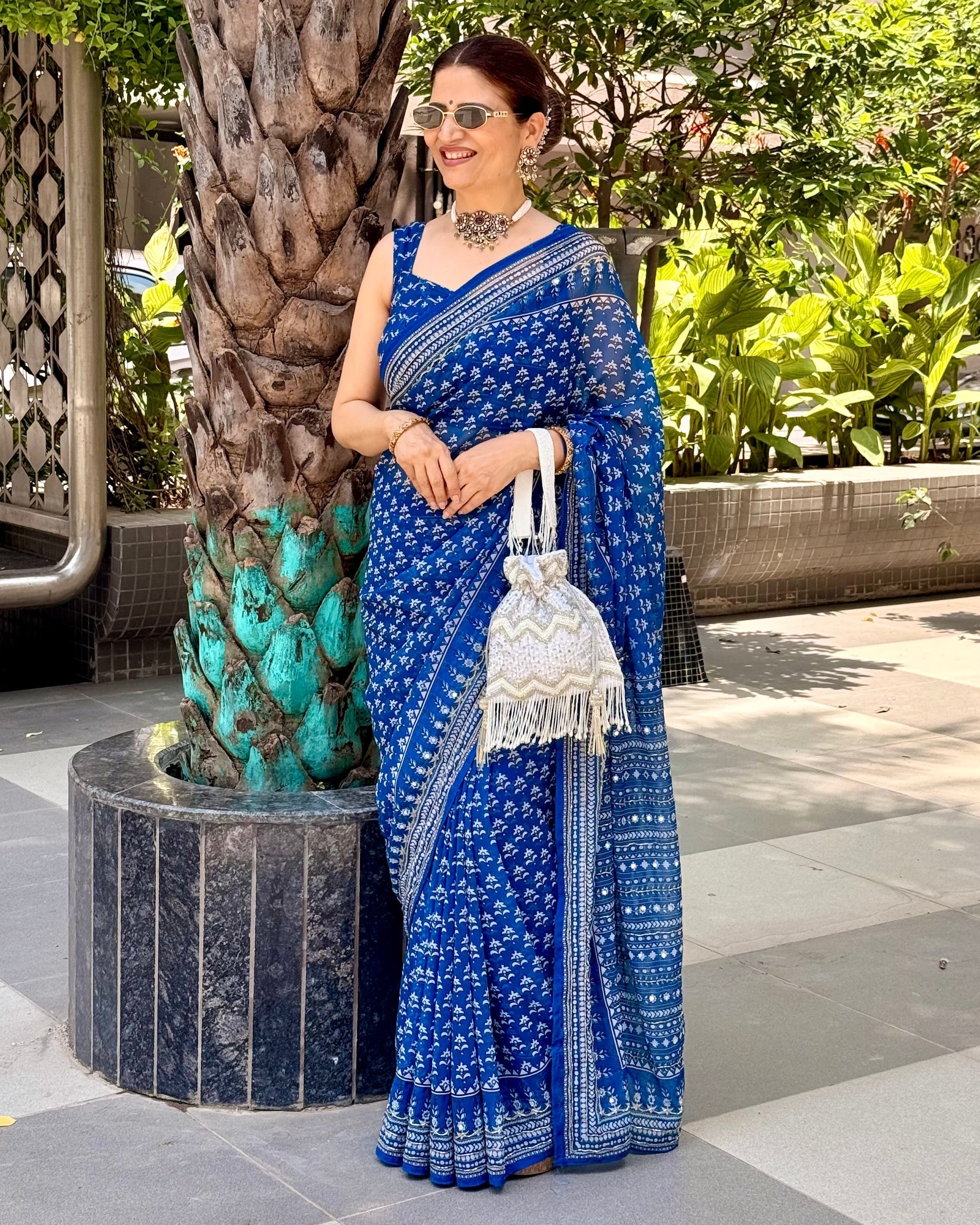 Woman in a blue saree standing next to a tree in an outdoor setting